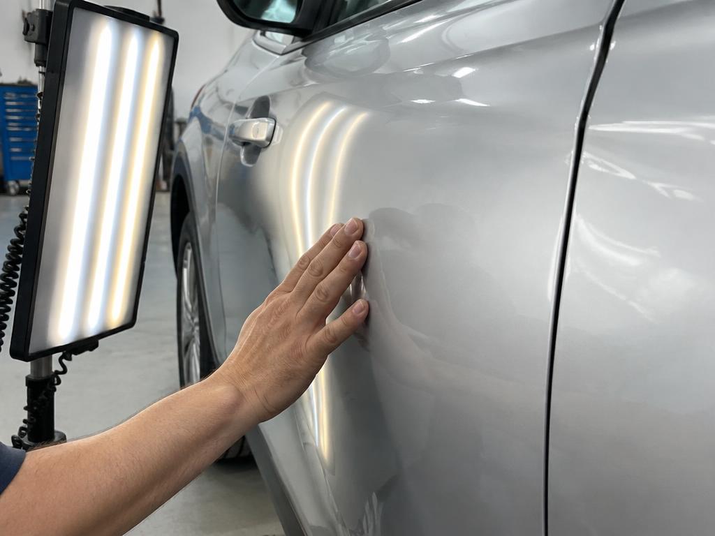 Technician inspecting a dent on a silver car door under a light board